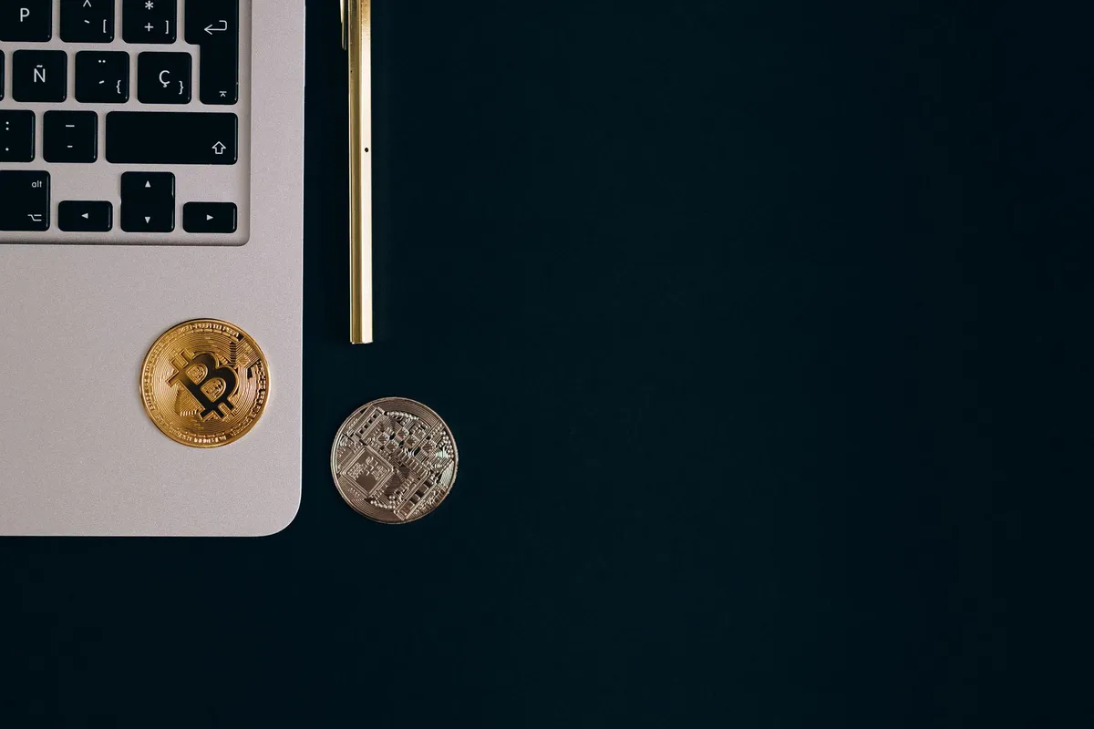 img-007.webp Close-up view of Bitcoin and Ethereum coins next to a laptop and pen on a black surface.