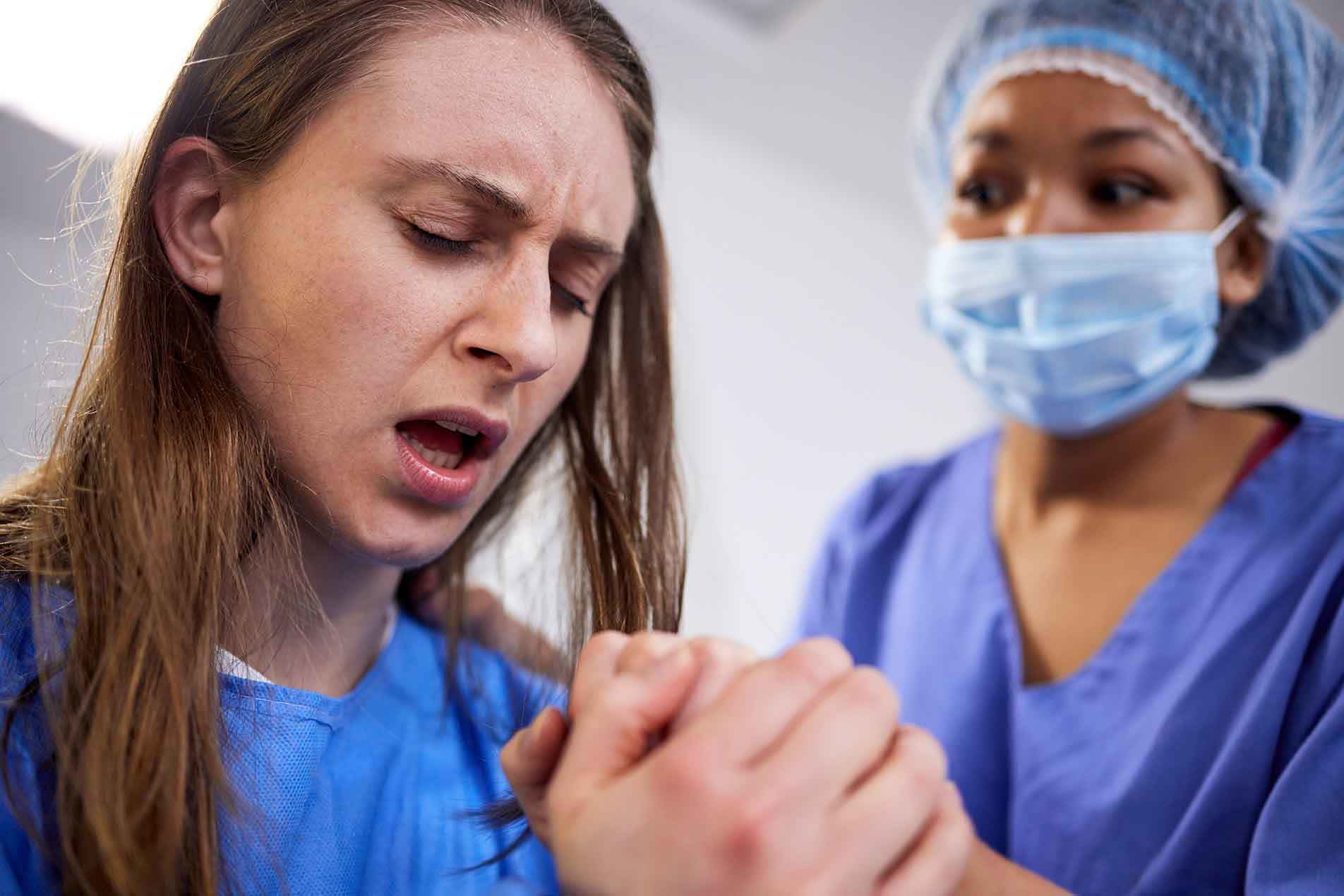 Eine Krankenschwester hält die Hand einer schmerzgeplagten Frau, um sie zu beruhigen.