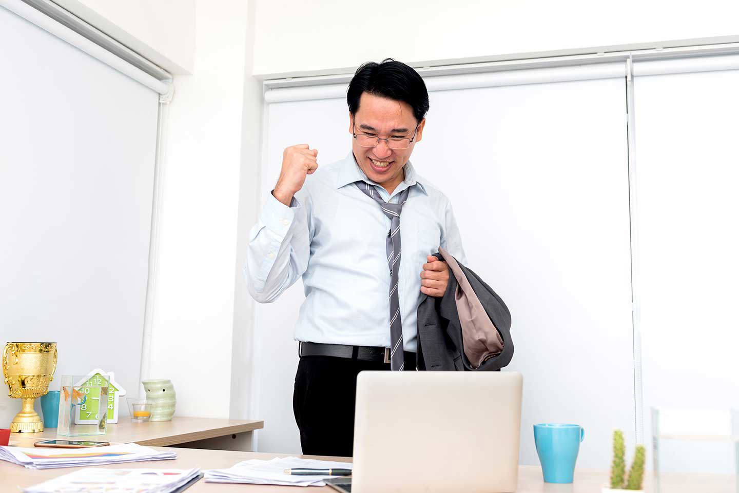 Geschäftsmann freut sich über einen Erfolg und jubelt vor seinem Laptop im Büro.