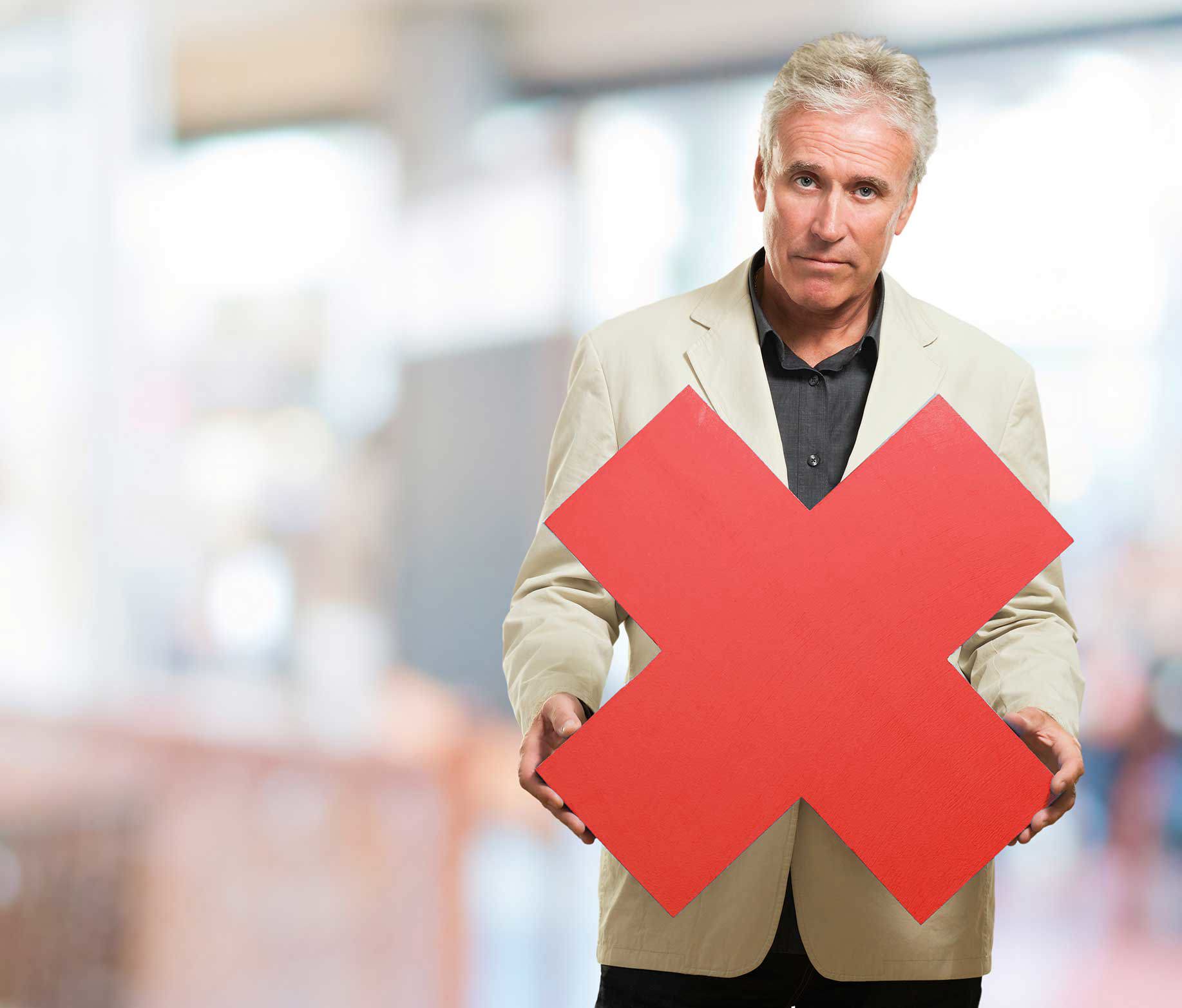 Un bărbat cărunt, cu privire serioasă, îmbrăcat într-un sacou deschis la culoare și o cămașă închisă, ține în fața sa un simbol mare de cruce roșie. Fundalul este neclar și pare a fi un interior. Crucea roșie simbolizează respingere, interdicție sau „Nu“.