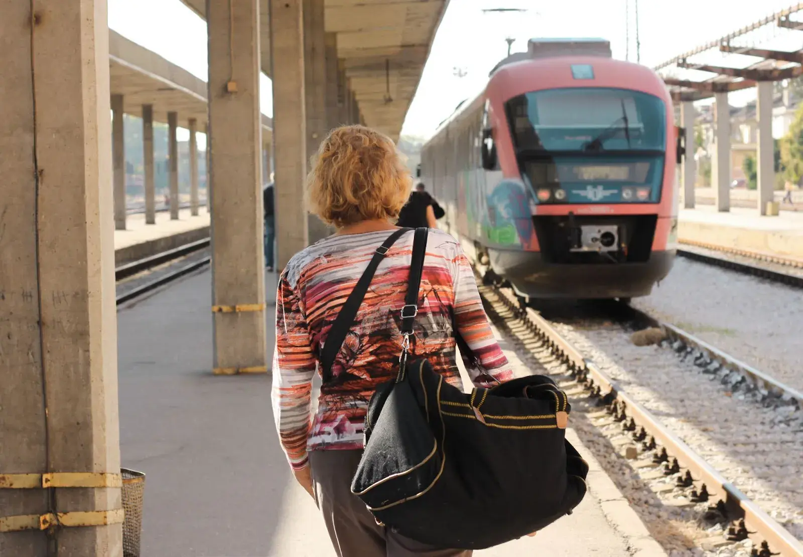 Frau mit großer Tasche geht über den Bahnsteig auf einen einfahrenden Zug zu