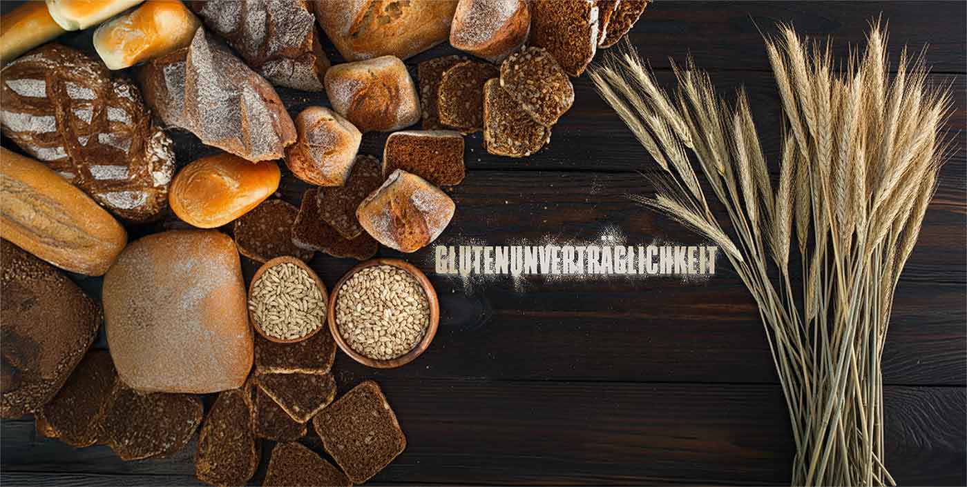 Verschiedene Brotsorten, Getreidekörner und Weizenähren auf dunklem Holzuntergrund mit dem Schriftzug Glutenunverträglichkeit