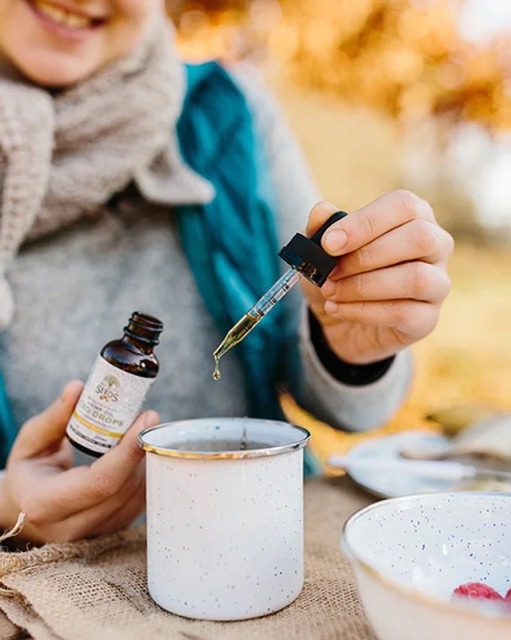 Frau hält eine Flasche und tropft Kräutertropfen in eine Emaille-Tasse