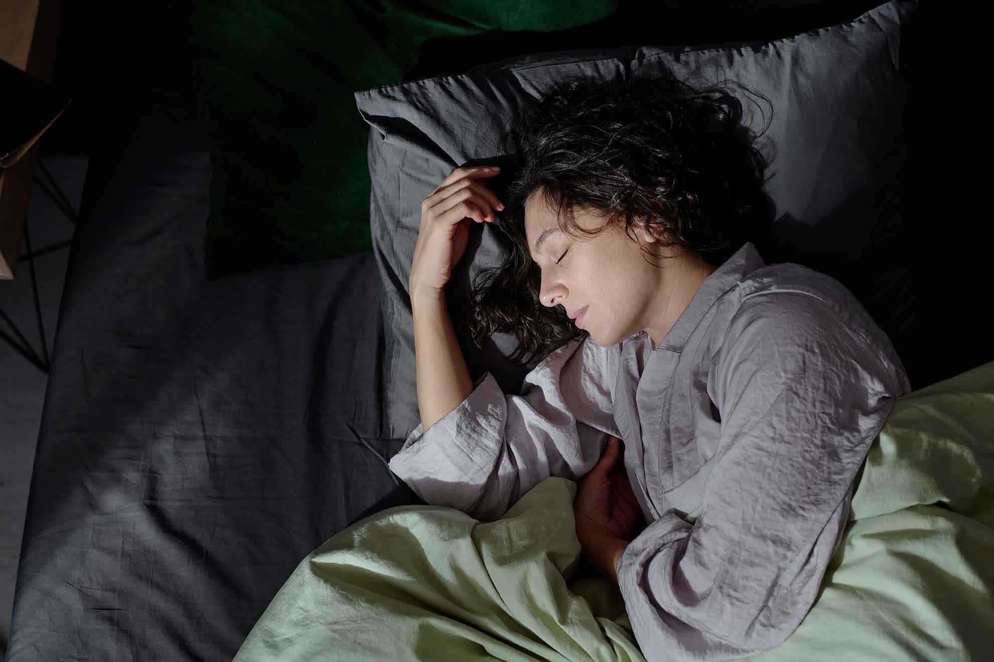 „Schlafende Frau liegt entspannt im Bett auf der Seite, zugedeckt mit einer Decke; ruhige Nachtszene im Schlafzimmer.“