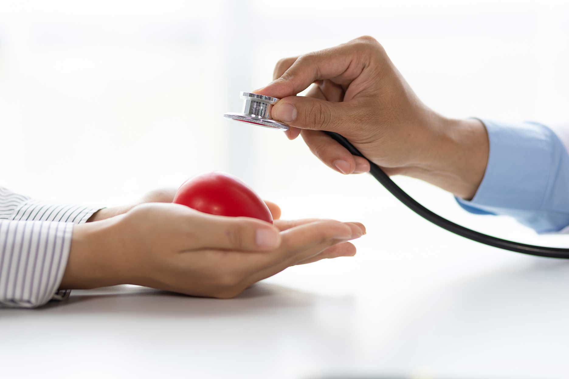 Ein Arzt, der mit einem Stethoskop eine rote Herz-Symbolfigur untersucht, die von einer Hand gehalten wird, um die Bedeutung der Herzgesundheit zu veranschaulichen.