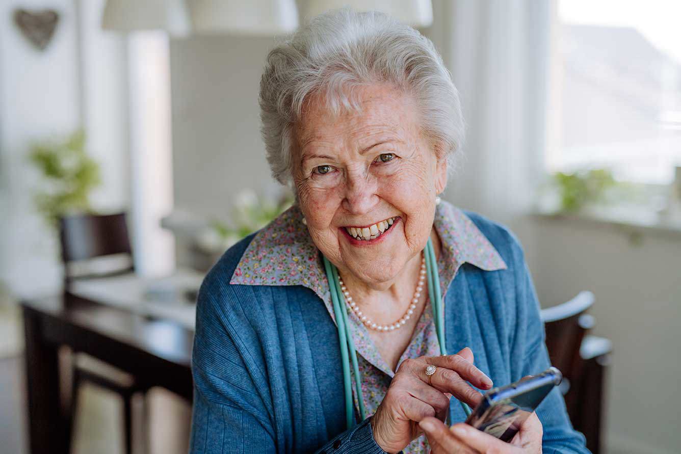 Ältere Frau lächelt und nutzt ihr Smartphone, um mit Familie und Freunden in Kontakt zu bleiben.