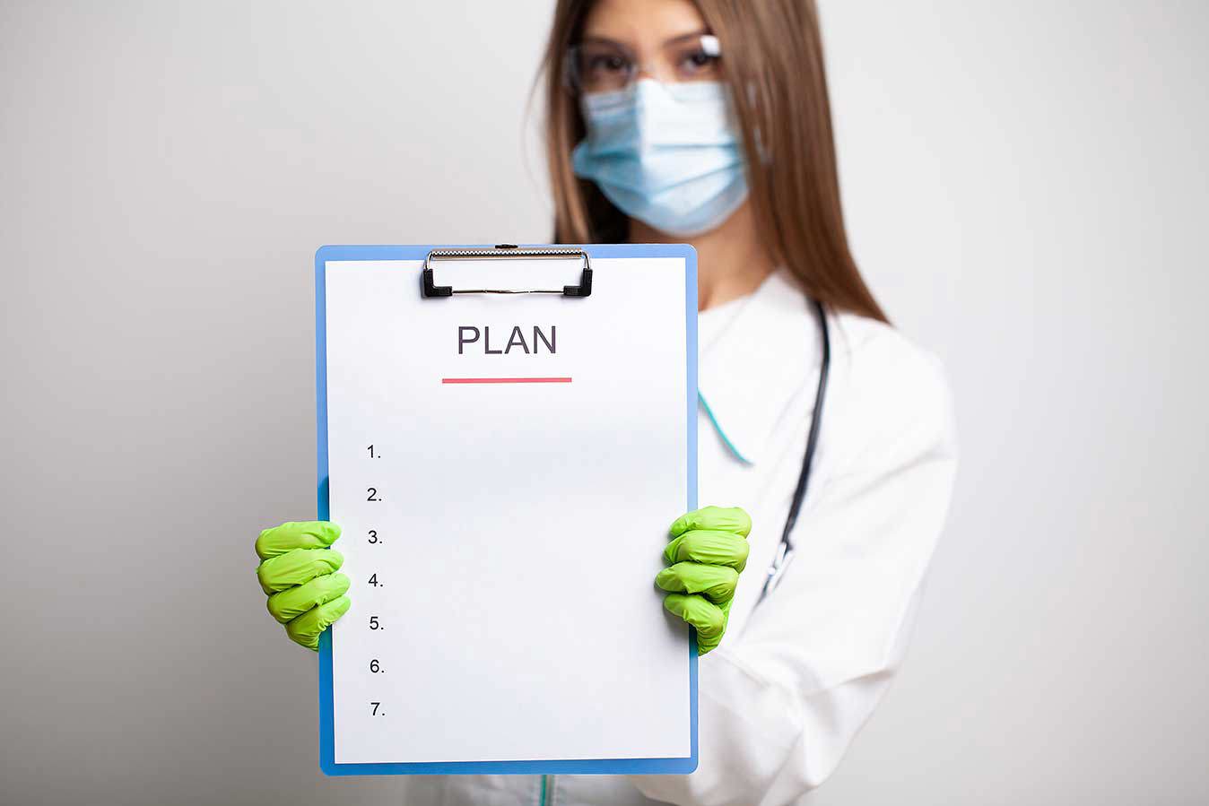 Un medic sau o asistentă în halat alb, cu mască și mănuși verzi, ține în mână un clipboard cu titlul
