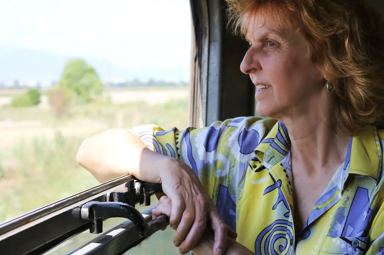 Ältere Frau schaut entspannt aus dem Fenster eines Zuges und genießt die vorbeiziehende Landschaft.
