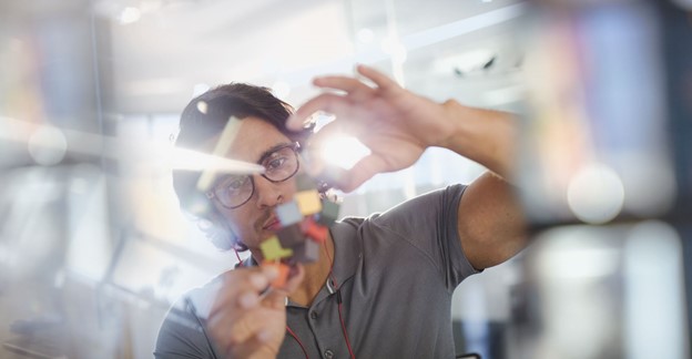 A person putting together a multicolored puzzle vertically facing the camera on a clear pane of glass