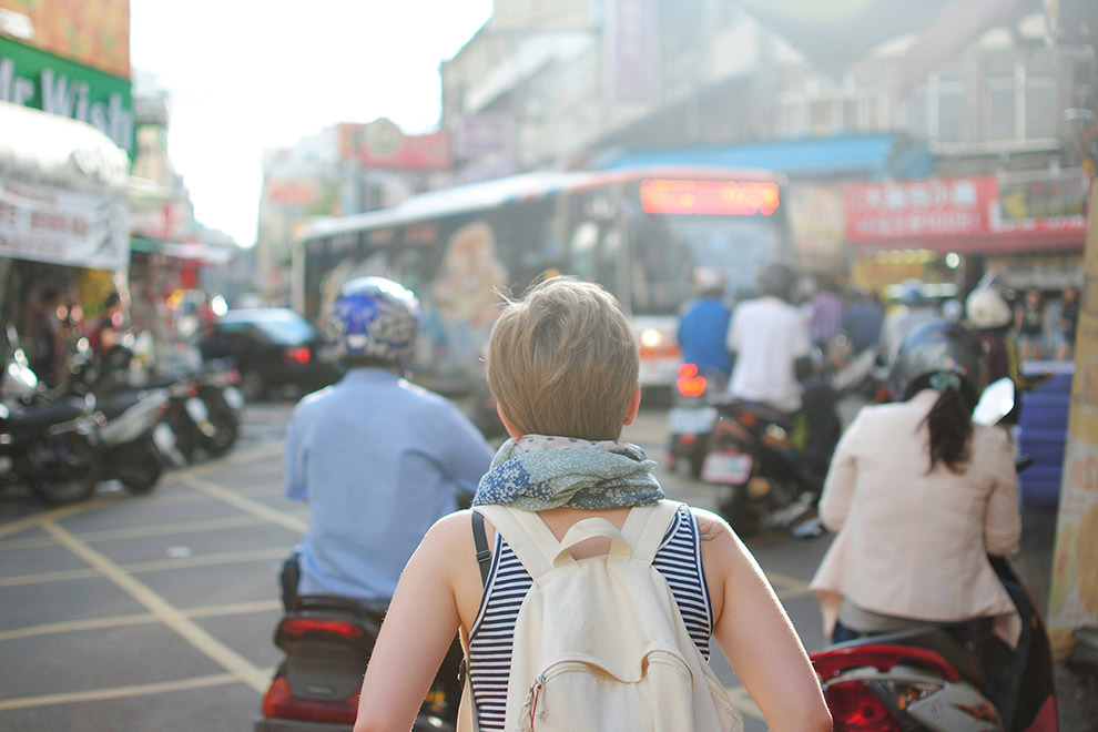 A person wearing a backpack looks at the crowd of people and streets in front of them.