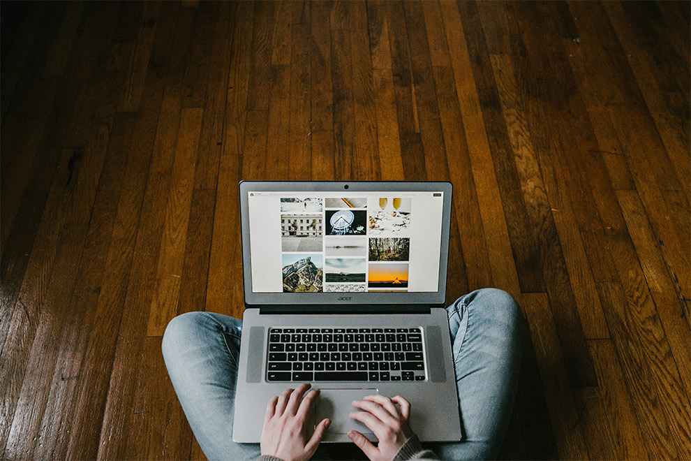 A person sits cross-legged on the ground, working on their blog on their laptop.