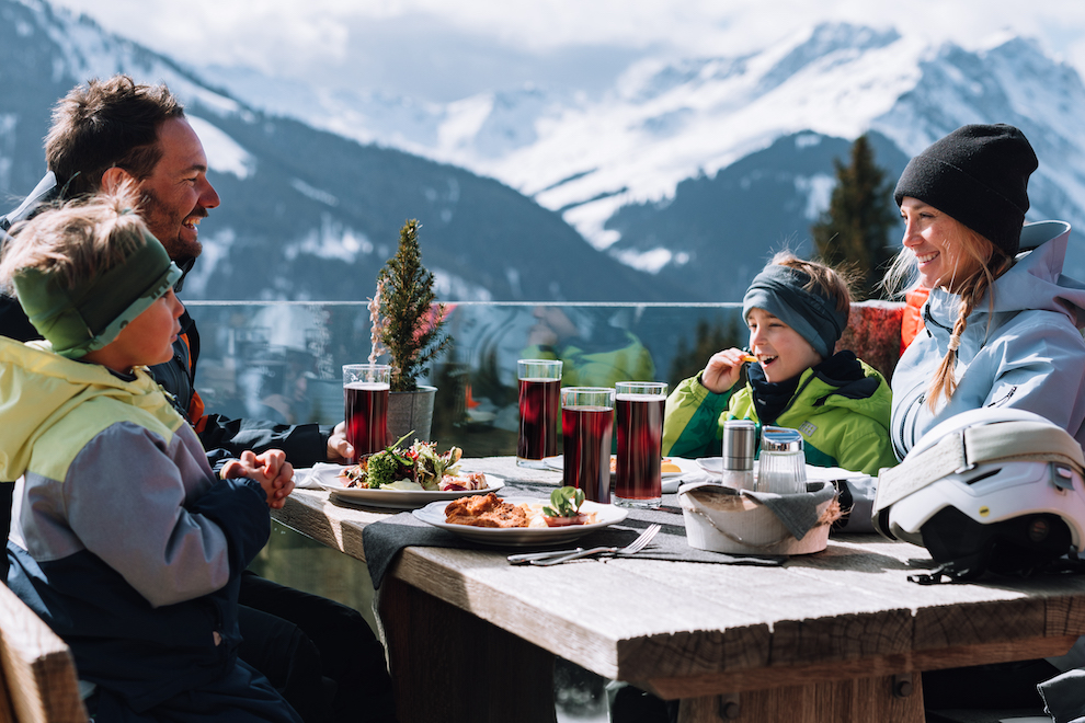Familie eet lunch op zonnige winter terras in Oostenrijk