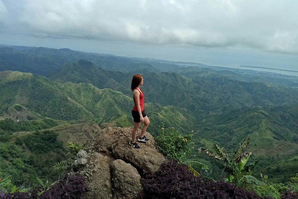 A woman standing at the top of a hill overlooking the vast green forest.