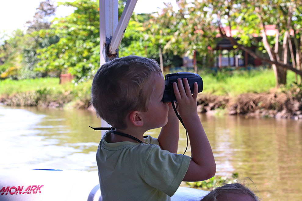 Zoontje kijkt door verrekijker op boot in Costa Rica