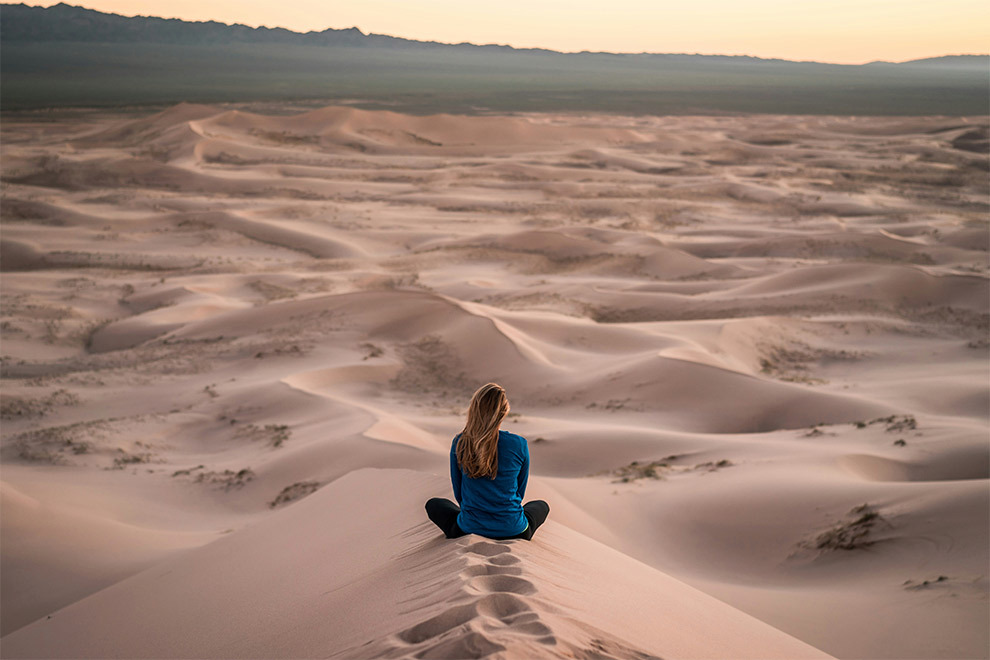 A woman sitting relaxed in the desert sand.