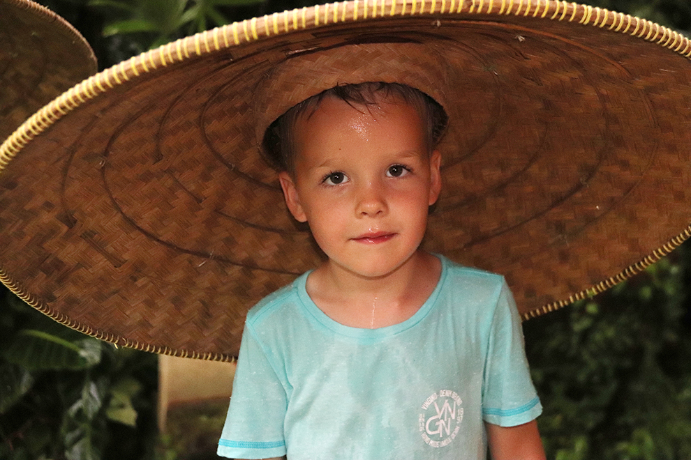Zoontje draagt hoed die dient als paraplu in Bali