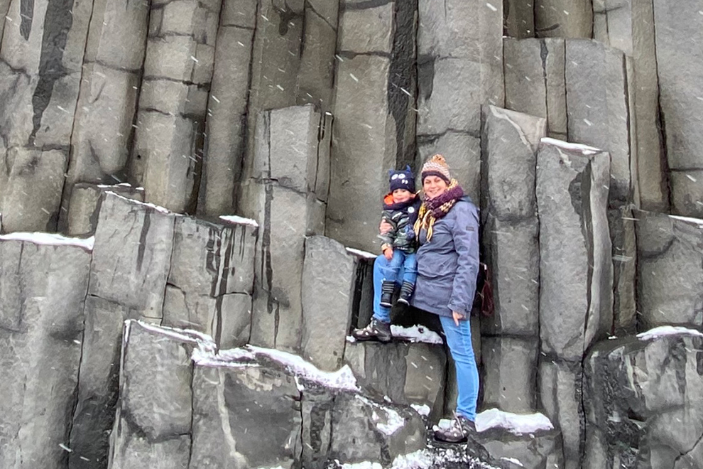 Moeder en zoon balanceren op basaltblokken in Reynisfjara, IJsland