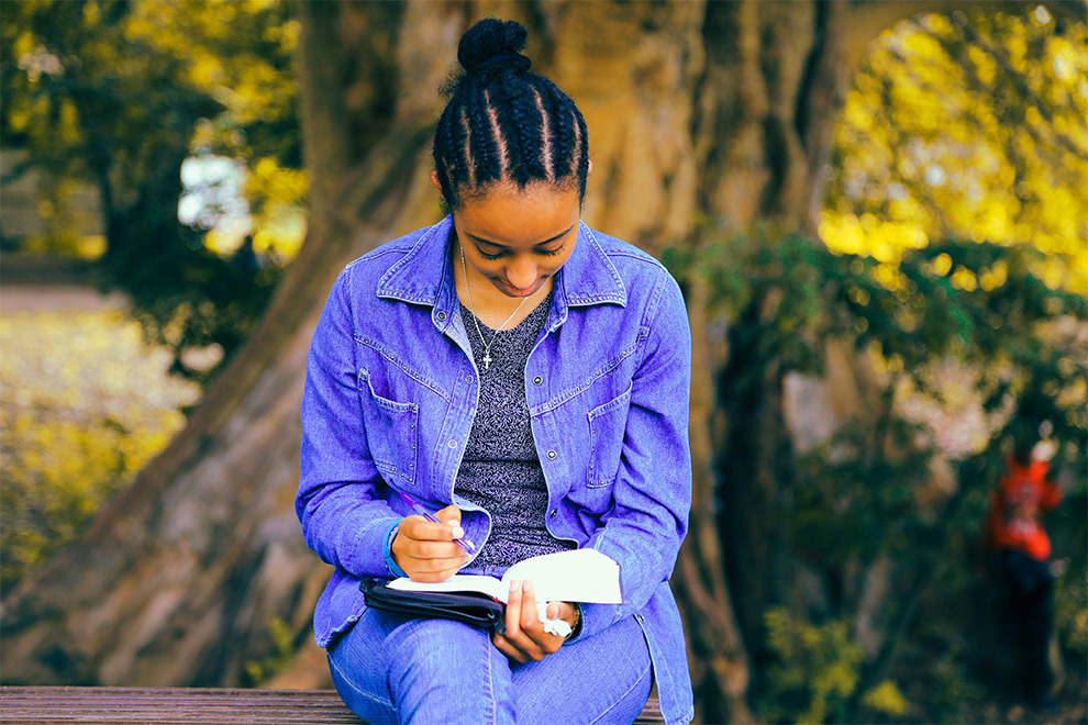 A woman sitting outside and writing in her diary.