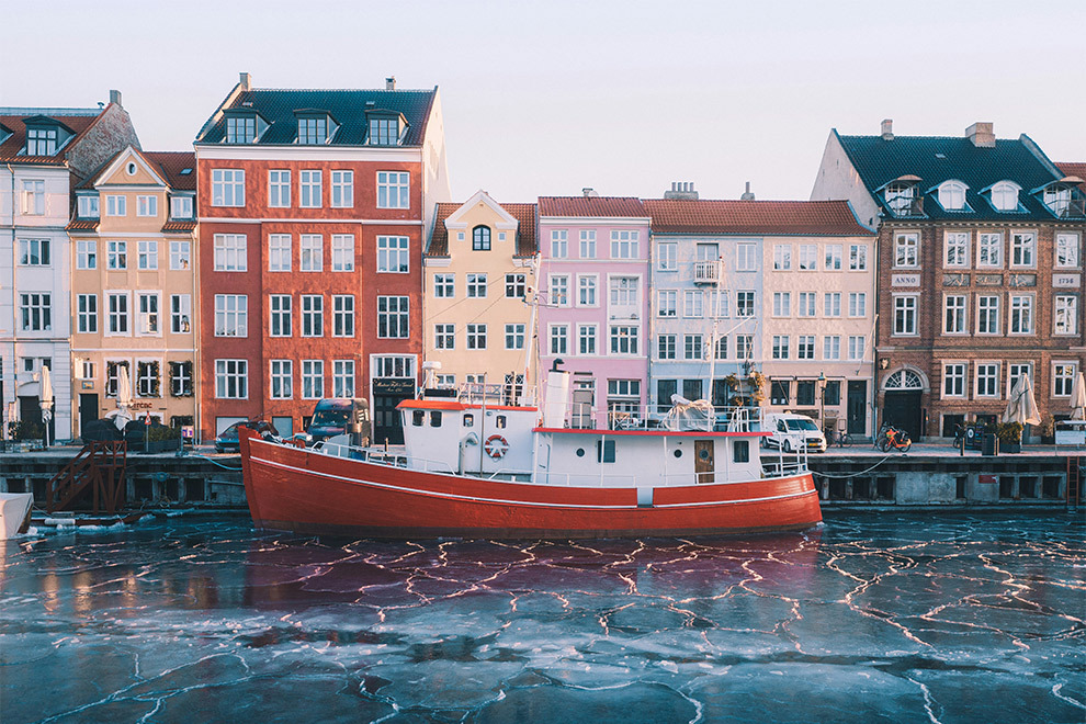 Een boot op de ijzige wateren van de Nyhavn met als achtergrond een regenboog aan kleurrijke huizen.