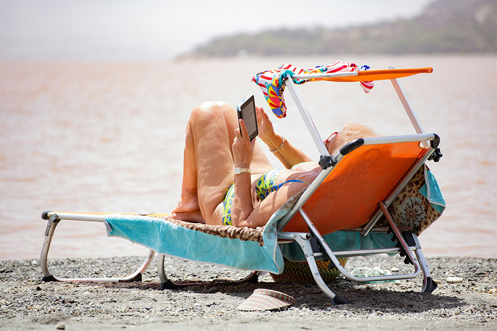 A woman lays on the beach, reading on her tablet.